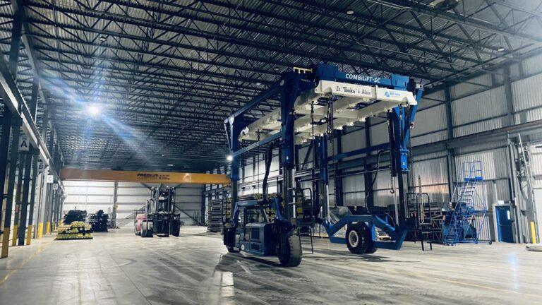Un grand entrepôt intérieur avec de hauts plafonds contient des machines industrielles, dont un chariot élévateur à fourche et un portique bleu sur roues.